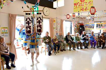 踊りながら会場入りする八千代連の踊り手たち。ただ今から、この機能訓練室は徳島県になります！